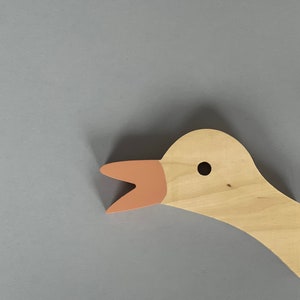 Op de afbeelding: Een houten ganzenkop met een lichtbruin lichaam en een roze snavel. De gans heeft een klein zwart oog.