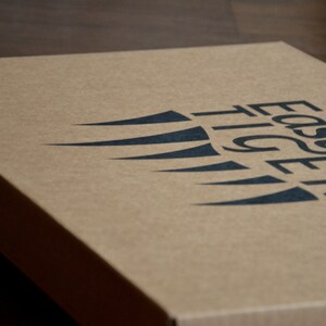 May include: A brown cardboard box with the words "Easy Tiger" printed in black letters. The logo features a stylized black wing design.
