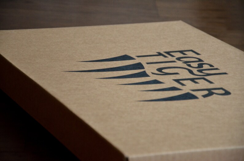 May include: A brown cardboard box with the words "Easy Tiger" printed in black letters. The logo features a stylized black wing design.
