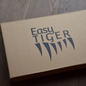 May include: A brown cardboard box with the words "Easy Tiger" printed in black on the top. The logo also includes a stylized black tiger claw print.