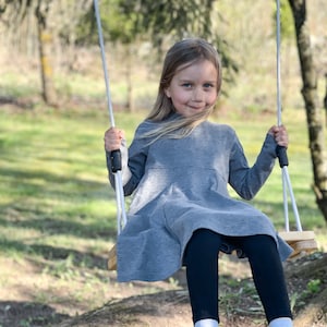 Girl joyfully swinging on a solid Wooden Tree Swing, perfect for kids and adults. This high-quality wood swing is built to last, offering years of enjoyment. Ideal for various occasions like weddings, birthdays, and Christmas.