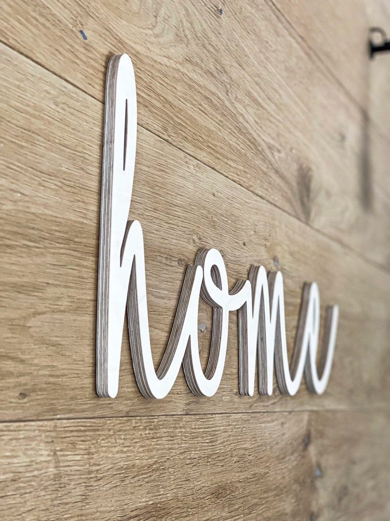 Może przedstawiać: Białe drewniane litery tworzące słowo "home" na tle drewnianego panelu.