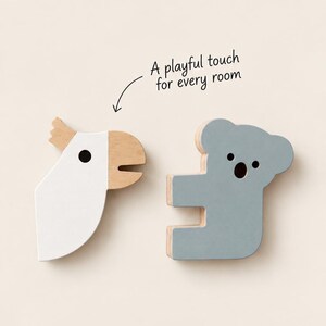 Può includere: Due decorazioni da parete in legno a forma di animale: un cacatua bianco con becco in legno naturale e un koala grigio. Entrambi presentano semplici occhi neri circolari. Sopra il cacatua, il testo recita: A playful touch for every room.