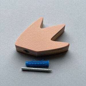 Op de afbeelding: Een lichtroze houten wanddecoratie in de vorm van een vogelpoot met een schroefgat. Een blauwe plastic wandplug en een zilveren schroef zijn inbegrepen.