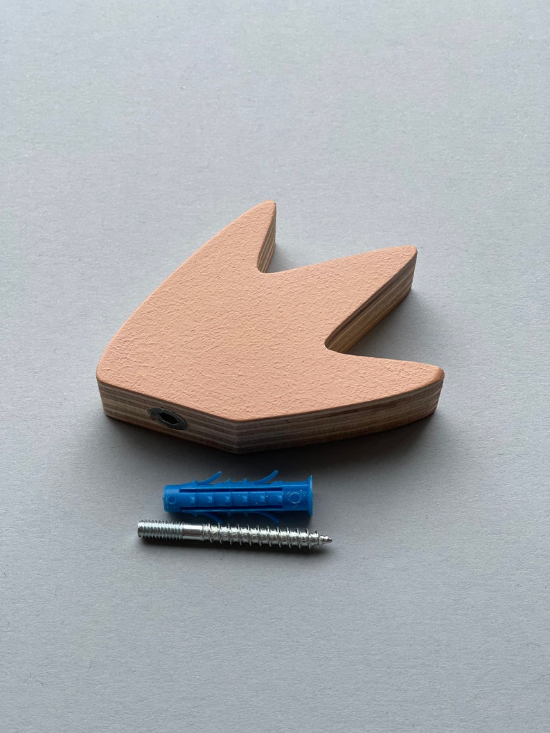Op de afbeelding: Een lichtroze houten wanddecoratie in de vorm van een vogelpoot met een schroefgat. Een blauwe plastic wandplug en een zilveren schroef zijn inbegrepen.