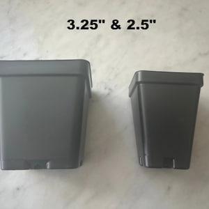 May include: Two dark gray square plant pots with a smooth finish. The larger pot is labeled 3.25 inches and the smaller pot is labeled 2.5 inches. Both pots feature a tapered design with a wide rim at the top and a narrow base, constructed from plastic.