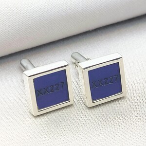 May include: A pair of silver cufflinks with a square blue inset. The inset has the text "XX227" engraved on it.
