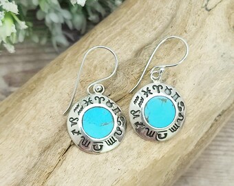 May include: A pair of silver dangle earrings with turquoise stones. The earrings feature a circle with the astrological signs around the edge.