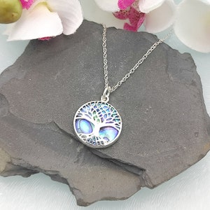 May include: A silver necklace with a round pendant featuring a tree of life design. The pendant is made of abalone shell with iridescent blue, green, and purple colours.