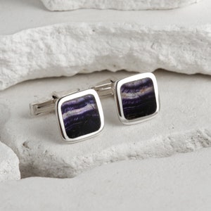 May include: A pair of silver cufflinks with square-shaped blue and purple fluorite stone inlays.