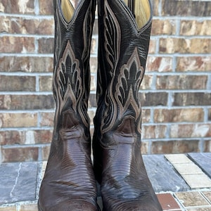 Op de afbeelding: Een paar donkerbruine leren cowboylaarzen met een textuur van hagedissenhuid op de voet en een schacht van glad leer met gedetailleerde crèmekleurige stiksels. De laarzen hebben een hoog model en een puntige neus.