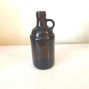May include: A dark brown glass bottle with a handle. The bottle has a rounded body and a narrow neck.