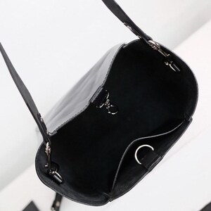 Puede incluir: Bolso tipo cubo de cuero negro con una correa larga para el hombro y una bolsa m&aacute;s peque&ntilde;a adjunta. El bolso tiene herrajes plateados y un dise&ntilde;o simple y minimalista. El interior tiene un peque&ntilde;o bolsillo.