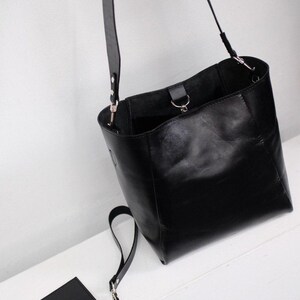 Puede incluir: Un bolso tipo cubo de cuero negro con una correa larga para el hombro y una bolsa m&aacute;s peque&ntilde;a a juego. El bolso tiene un dise&ntilde;o simple y minimalista con herrajes plateados. El bolso mide aproximadamente 30 cm de alto.