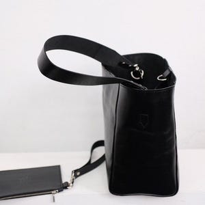 Puede incluir: Bolso tote de cuero negro con una peque&ntilde;a bolsa a juego. El bolso tiene un asa &uacute;nica y una correa de hombro desmontable. El bolso es rectangular con un dise&ntilde;o estructurado y herrajes plateados.