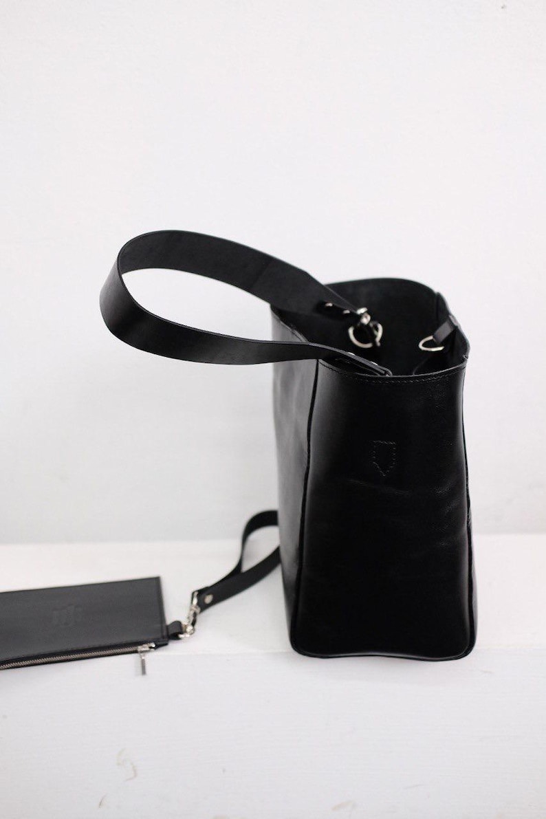 Puede incluir: Bolso tote de cuero negro con una peque&ntilde;a bolsa a juego. El bolso tiene un asa &uacute;nica y una correa de hombro desmontable. El bolso es rectangular con un dise&ntilde;o estructurado y herrajes plateados.