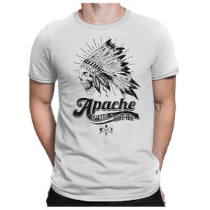 May include: A white t-shirt with a black and white graphic of a skull wearing a Native American headdress. The graphic includes the text "Apache Apparel Since 1905" and a compass.
