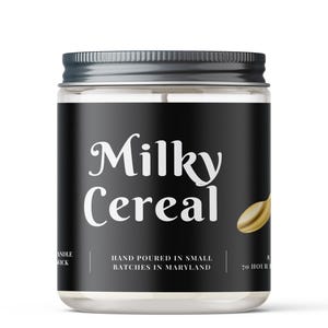 May include: A clear glass jar with a silver lid, featuring a black label with the words "Milky Cereal" in white script. A golden cereal graphic is on the right. The label also states "Hand Poured in Small Batches in Maryland".
