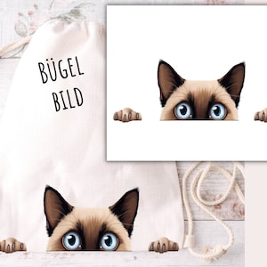 Può includere: Una borsa tote in tela bianca con il testo "Bügel Bild" stampato su di essa. Un gatto siamese sporge la testa sopra la borsa con le zampe su entrambi i lati.