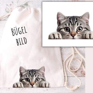 May include: A white drawstring bag with the text "BÜGEL BILD" printed on the front. A grey tabby cat is peeking over the top of the bag.