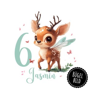May include: A cute cartoon deer with fairy wings and a light brown and white spotted body. The deer is standing on a green patch of grass with pink flowers. The number 6 is in the background in a light blue colour. The text "Jasmin" is written below the deer in a light blue colour. The text "BÜGEL BILD" is in a black circle in the lower right corner.
