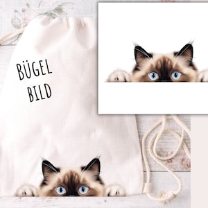 Peut inclure: Un sac à cordon blanc avec le texte "BÜGEL BILD" imprimé sur le devant. Un chat aux yeux bleus regarde par-dessus le sac.