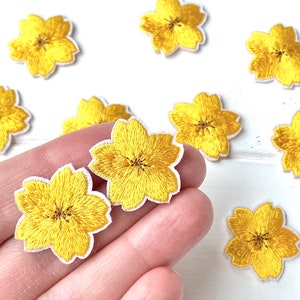 Könnte beinhalten: Zehn gelbe Filzblumen-Patches mit weißen Nähten. Die Blumen sind auf einer weißen Oberfläche angeordnet.