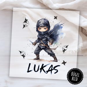 Peut inclure: Illustration à l'aquarelle d'un ninja en tenue noire, tenant une épée. L'image présente le nom "LUKAS" en gras. Des shurikens et des éclaboussures d'encre entourent le ninja, avec un autocollant "BÜGEL BILD" dans le coin.