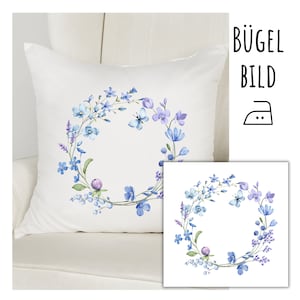 May include: Iron-on transfer design featuring a wreath of blue and purple watercolor flowers with a butterfly in the center. The design is on a white background and says "Bügel Bild" in the top right corner.