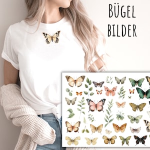 Könnte beinhalten: Ein weißes T-Shirt mit einem Aquarell-Schmetterlingsdesign. Das Bild zeigt auch eine Folie mit Bügelbildern von Schmetterlingen in verschiedenen Farben und Mustern. Der Text "Bügel Bilder" ist in der oberen rechten Ecke des Bildes sichtbar.