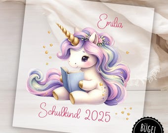 Könnte beinhalten: Bügeleisen-Transfer mit einem lila und pinkfarbenen Einhorn, das ein Buch liest. Das Einhorn hat ein goldenes Horn und eine Blumenkrone. Der Text "Emilia Schulkind 2025" befindet sich unterhalb des Einhorns.