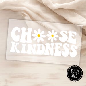 Può includere: Decalcomania in vinile bianco con le parole "CHOOSE KINDNESS" in un font retrò, con accenti di fiori di margherita. La decalcomania è su uno sfondo trasparente, con un adesivo in bianco e nero nell'angolo in basso a destra.