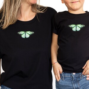 May include: Matching black t-shirts with a green butterfly graphic. The adult shirt is larger than the child's shirt.