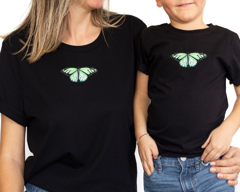 May include: Matching black t-shirts with a green butterfly graphic. The adult shirt is larger than the child's shirt.