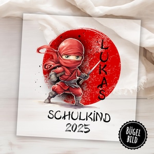 May include: Red and white iron-on transfer design featuring a cartoon ninja with a red headband and a sword. The design also includes the name "LUKAS" and the text "SCHULKIND 2025".