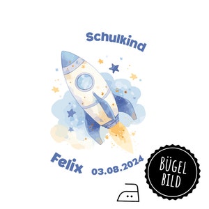 May include: A blue and white rocket ship with a yellow flame, surrounded by blue and white clouds and gold stars. The text "Schulkind" is above the rocket, and the text "Felix 03.08.2024" is below the rocket. A black circle with the text "BÜGEL BILD" is in the lower right corner of the image.