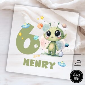 Op de afbeelding: Vierkante, lichtgekleurde print met een vriendelijke groene alien, planeten, sterren en de naam "HENRY". Het cijfer 6 is groen. De print heeft een aquarel stijl en een ruimtethema.