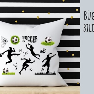 Può includere: Un cuscino bianco con silhouette nere di giocatori di calcio, un pallone da calcio e la parola "SOCCER" stampata su di esso.