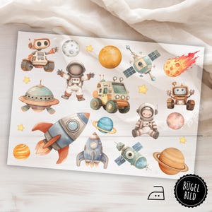 Könnte beinhalten: Ein Bogen mit Weltraum-Stickern mit Raketen, Planeten, Astronauten, Robotern und einem UFO. Die Aufkleber sind in Blau-, Orange- und Beigetönen gehalten und haben einen Aquarell-Effekt. Der Bogen enthält ein schwarz-weißes Bügeleisensymbol und einen runden Aufkleber mit dem Text "BÜGEL BILD".