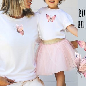 May include: Two white t-shirts with pink butterfly iron-on designs. The text "B&Uuml;GEL BILDER" is visible in the background.