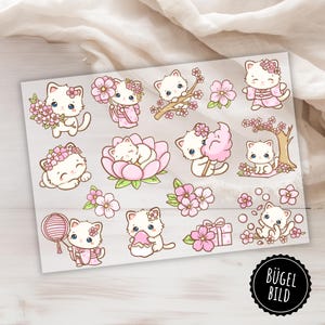 May include: A sheet of iron-on transfer stickers featuring 15 adorable white kittens with pink accents. The kittens are depicted in various poses, including sleeping, holding flowers, and wearing traditional Japanese clothing. The stickers are perfect for adding a touch of whimsy to clothing, bags, or other fabric items.