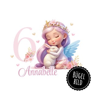Op de afbeelding: Een roze en witte illustratie van een fee met vleugels die een wit konijn vasthoudt. De fee heeft een kroon op haar hoofd en draagt een roze jurk. Het getal 6 staat op de achtergrond en de naam Annabelle staat onder de fee. De woorden "Bügel Bild" staan in een zwarte cirkel rechtsonder in de afbeelding.
