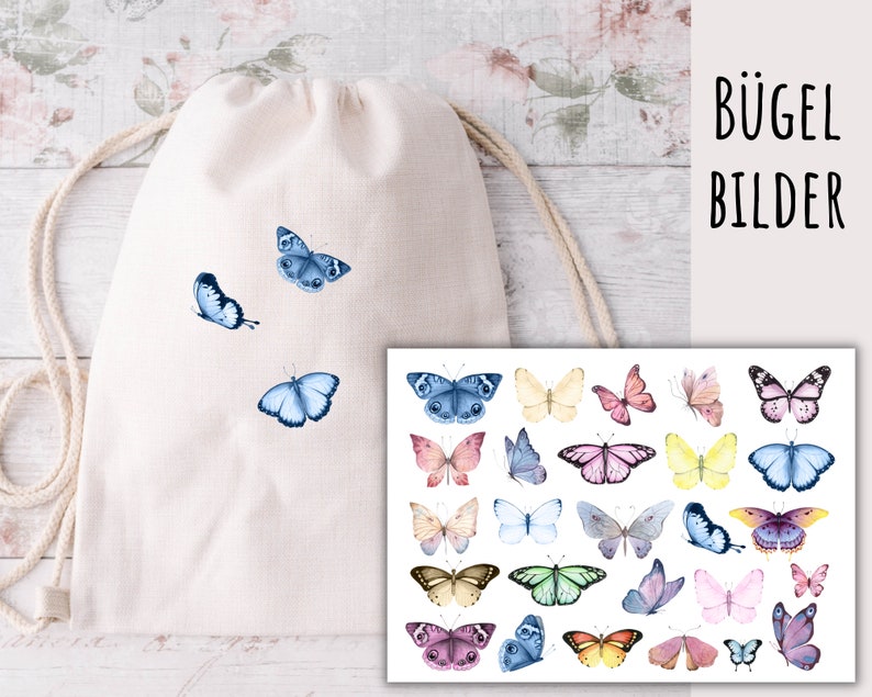 May include: A white drawstring bag with blue butterfly iron-on transfers. The bag is lying on a white wooden surface. A sheet of paper with colorful butterfly iron-on transfers is shown next to the bag. The paper has the text "B&uuml;gel Bilder" printed on it.