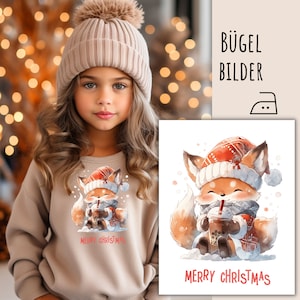 Op de afbeelding: Een meisje draagt een beige sweatshirt met een aquarel vos. De vos draagt een kerstmuts en sjaal, houdt een drankje vast en daaronder staat "MERRY CHRISTMAS". Rechts is een vergelijkbare afbeelding te zien. De tekst "BÜGEL BILDER" is ook zichtbaar.