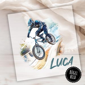 May include: A watercolor illustration of a person riding a BMX bike on a ramp. The person is wearing a helmet and protective gear. The name "LUCA" is written in blue text below the bike. The words "BÜGEL BILD" are in a circle at the bottom right corner of the image.