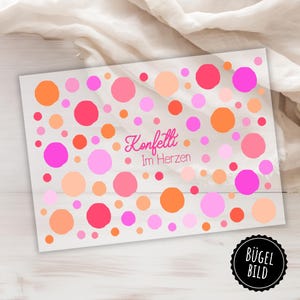 Könnte beinhalten: Bügelbild mit weißem Hintergrund und rosa, orangen und roten Punkten. Der Text "Konfetti Im Herzen" ist in rosa Kursivschrift geschrieben.