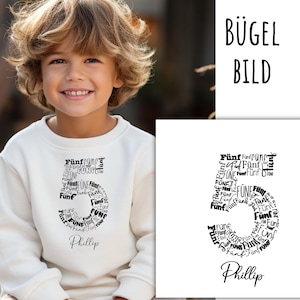 Op de afbeelding: Een crèmekleurige sweatshirt met een grote 5-afbeelding, samengesteld uit het woord "Fünf" in verschillende lettertypen. De naam "Phillip" staat in cursief onder het nummer. De woorden "BÜGEL BILD" staan rechtsboven.
