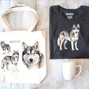 May include: A white tote bag with a watercolor illustration of Siberian Huskies. The bag has the text "Siberian Husky" printed on it. The tote bag is next to a dark gray t-shirt with a watercolor illustration of a Siberian Husky. A white mug is also in the image.
