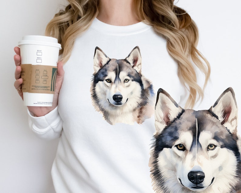 May include: White sweatshirt with a watercolor illustration of two husky dogs. The dogs are facing forward with their eyes open and their tongues out. The sweatshirt is a light white color and the dogs are a light gray and white color.