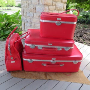 May include: Set of four red vintage suitcases with silver accents. The suitcases are stacked on top of each other, with the smallest suitcase on top.